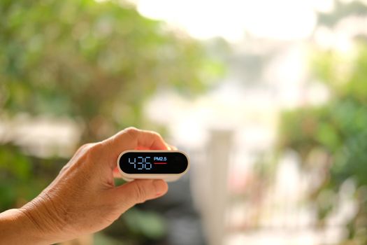 people hand holding pm 2.5 detector for checking air quality. air pollution from fine particle causing bad unhealthy weather