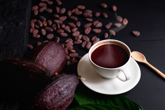 Hot chocolate and Cocoa pod cut exposing cocoa seeds on dark table, top view with copy space.