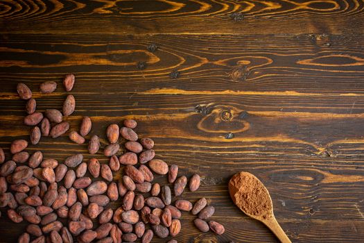 Cocoa beans and cocoa powder in wooden spoon on old natural wooden background.