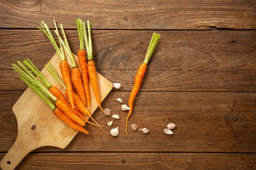 Fresh baby carrots on wooden cutting board and wooden background.