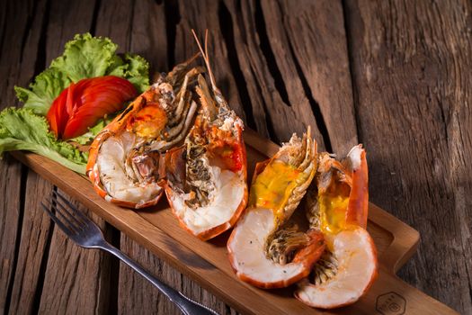 grilled giant river prawn with yellow creamy fat on head on a wooden plate.