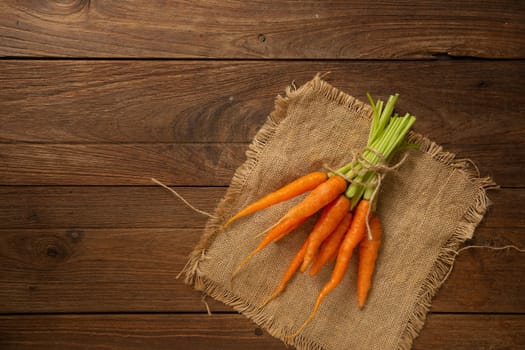 Fresh baby carrots on wooden cutting board and wooden background.