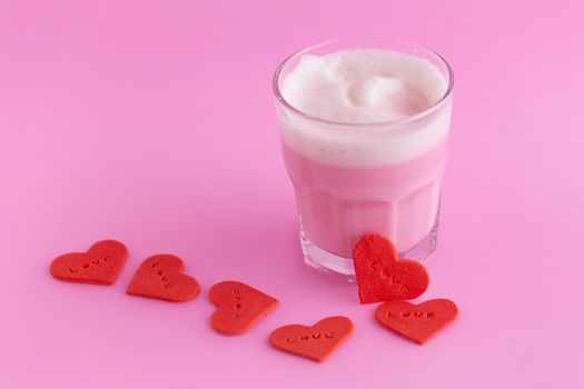 Strawberry milk shake from the glass and Red heart shaped sugar on pink background.