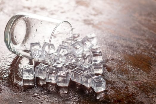 Glass of Ice cube on wooden table and light blurred background.