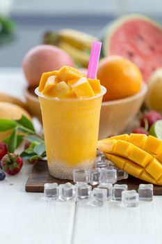 Ripe Mango Smoothies on a wooden plate with ice cubes and fruit as background.