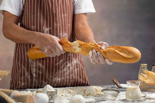 Chef holds the fresh bread in hand. Man preparing buns at table in kitchen.