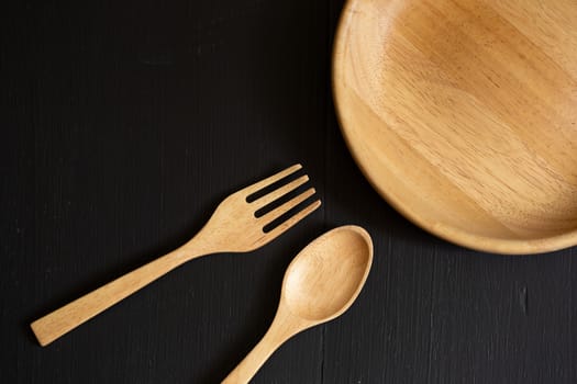 Spoons, forks and Dish made of wood on the black wooden background.