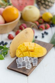Ripe Mango on a wooden plate with ice cubes and fruit as background.