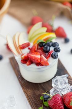 Healthy fruit salad with yoghurt on a wooden plate with ice cubes and fruit as background.