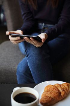 Asian female typing text message with coffe and Croissant