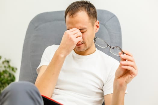 Man with tired eyes after long work holding his eyeglasses