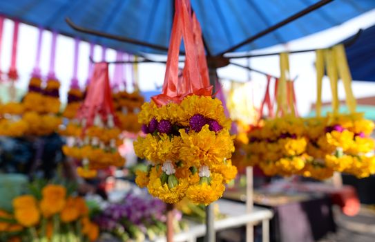 The garland is made of bright yellow flowers. Was hung for sale in the market, blurred background.