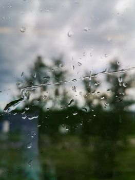 Long raindrops on window in train with trees in background