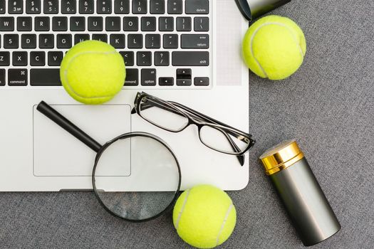 Top view of laptop, Sports Equipment, Tennis ball, Shuttlecock, glasses aon the Sports administration gray table.Business concept.