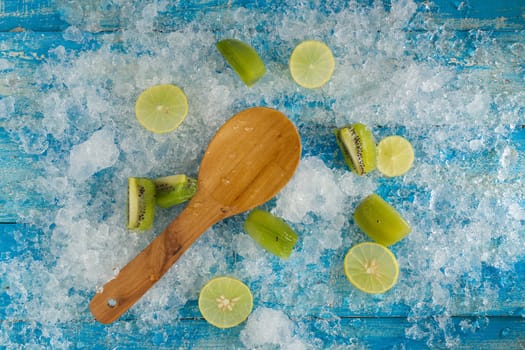 Crushed ice cubes and lemon, kiwi, wooden spoon on vintage blue wooden table. Top view.