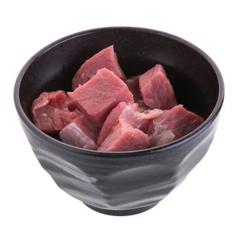 fresh raw beef cubes in black bowl isolated on white background.
