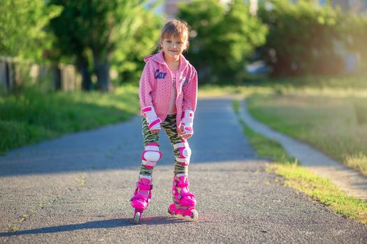 Little girl in pink rollers and pink sweater posing in the park and smiling. Happy child rollerblading. Children's sports and healthy lifestyle