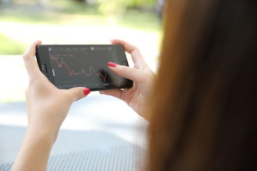 Female hand with smartphone trading stock online in outdoor coffee shop , Business concept