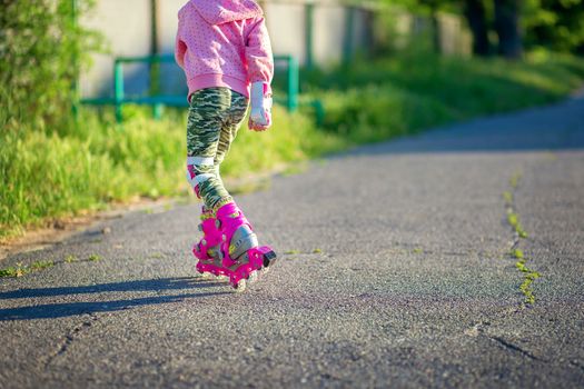 A little girl rides on pink roller skates on asphalt in the summer. The child learns to ride roller skates. Skating