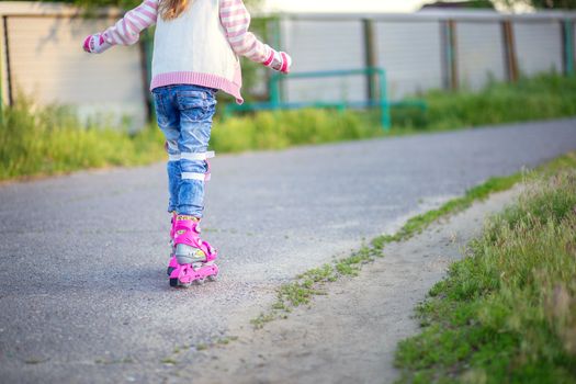 A little girl rides on pink roller skates on asphalt in the summer. The child learns to ride roller skates. Children's sports and healthy lifestyle