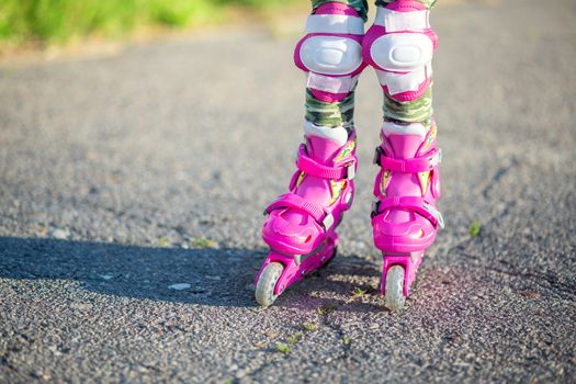 Childrens feet in pink childrens rollers close-up. Roller skates for outdoor sports. Healthy lifestyle baby