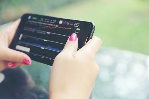 Female hand with smartphone trading stock online in coffee shop , Business concept