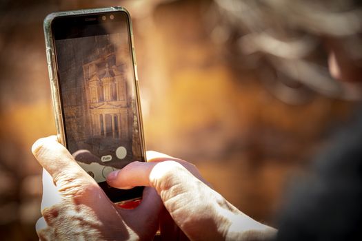 Tourist taking a picture with a smartphone, or mobile phone of The Treasury from the viewpoint in Petra, near Wadi Musa, Jordan