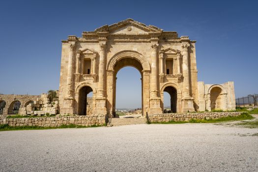 Arch of Hadrian at the roman ruins of Jerash, Jordan. Front view on a sunny day with blue sky. It features some unconventional, possibly Nabataean, architectural features, such as acanthus bases. Travel and Tourism in Jordan