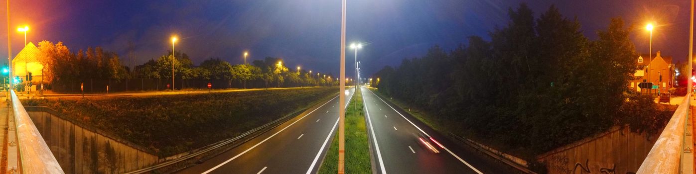 Panorama of an highway with a car driving by at night with lights turned on