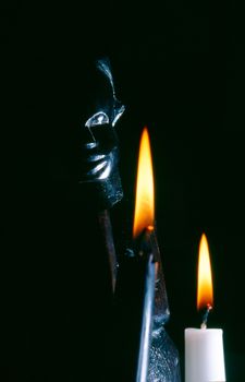 dark close-up image of an african statue with two burning candels