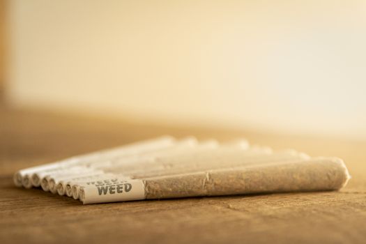 A bunch of Dutch Marijuana or weed joints next to each other, lined up, on rough wood, warm sunlight from the side.