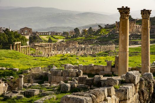 General view of the historical Roman site Gerasa in Jerash, Jordan, with pillars and Oval Plaza. Mountains and city in the far distance. Travel and Tourism in Jordan