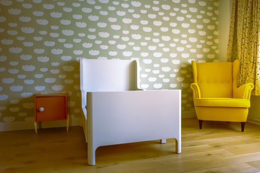 Toddler boy's sleeping room, with cloud pattern on wall, vintage chair, wooden floor and orange bedside table. Vintage look.