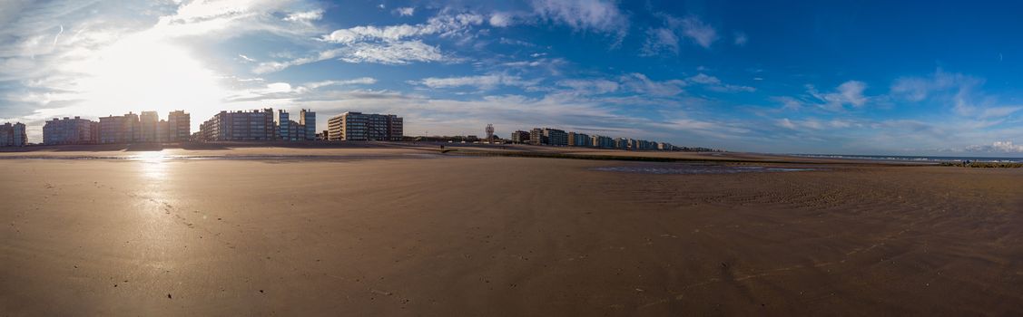 panoramic view on beach in autmunal light with a lot of sand in the foreground and the sun shinning in the background