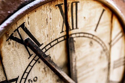 Old vintage and retro analogue clock displaying five minutes to twelve. Worn-out and grunge style with wooden background.