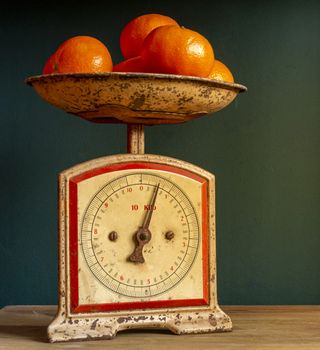 Weighing tangerines in a retro, vintage and worn out scale or balance, on a wooden plank against a guatemala green wall.