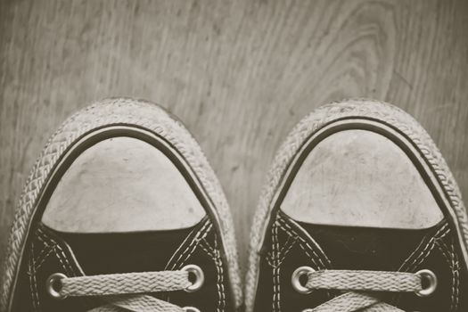 orn out converse Chuck Taylor All-Star sneakers tips, with black fabric, on wooden floor. Creative edit.