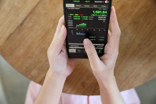 Female hand with smartphone trading stock online in coffee shop , Business concept