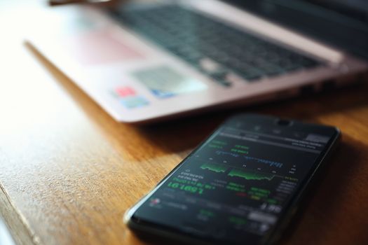 Female hand with smartphone trading stock online and notebook in coffee shop , Business concept