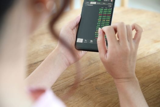 Female hand with smartphone trading stock online in coffee shop , Business concept