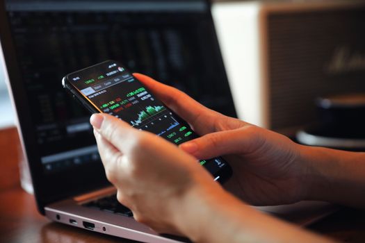 Female hand with smartphone trading stock online in coffee shop , Business concept