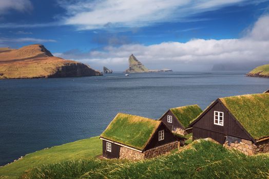 Village of Bour on Faroe Islands located on the coast of Atlantic Ocean with famous Drangarnir sea stack in the background.