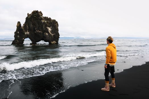 Tourist looks at the Hvitserkur basalt stack in northern Iceland. Hvitserkur is a spectacular rock in a shape of a dragon or dinosaur drinking water from the ocean.