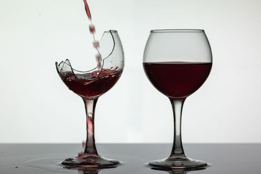 Wine. Red wine pouring into broken wine glass on the wet surface. Rose wine pour. Close up shot. White background