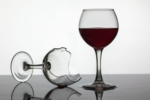 Filled with a glass of wine and broken wine glass with red wine which is laying on the wet surface. White background