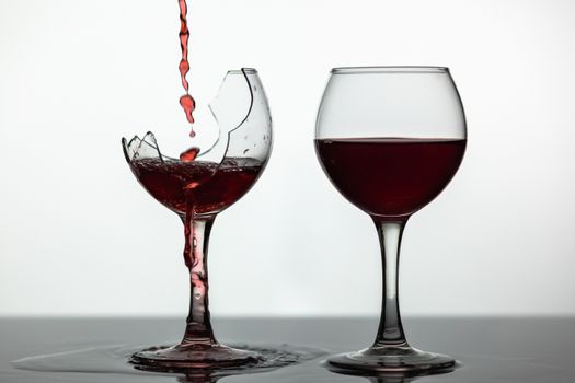 Wine. Red wine pouring into broken wine glass on the wet surface. Rose wine pour. Close up shot. White background