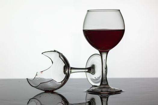 Filled with a glass of wine and broken wine glass with red wine which is laying on the wet surface. White background