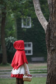 Portrait young woman with Little Red Riding Hood costume with apple and bread on basket in green tree park background