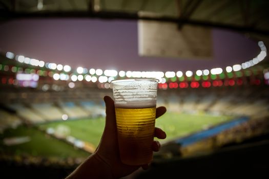 Disposable glass with beer. Soccer stadium on the background.