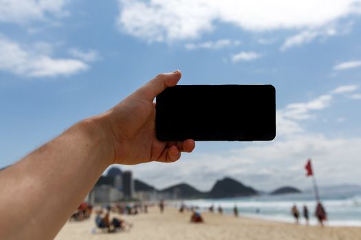 Using a smartphone on the beach. Blank black screen for your content